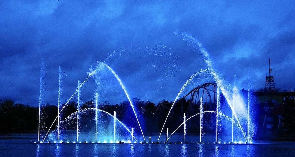 Illuminated blue water fountains against a cloudy night sky.