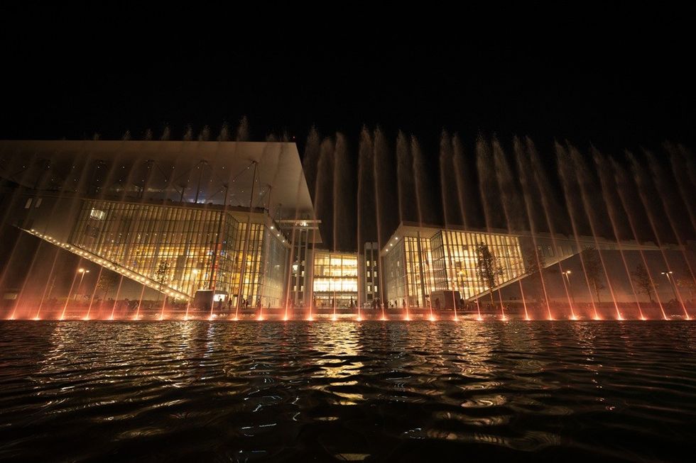 Illuminated building at night with tall water fountains in the foreground.