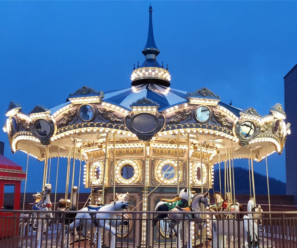Illuminated carousel with horses against a twilight sky.