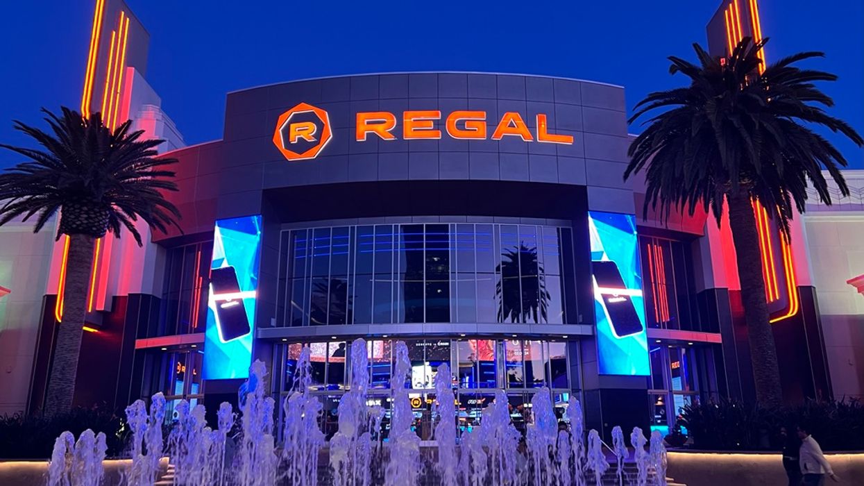 Illuminated cinema entrance with fountains and palm trees at night.