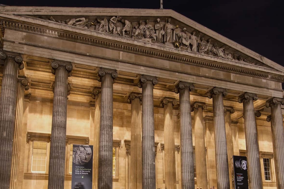 Illuminated classical building facade of the British Museum with tall columns and detailed frieze at night.