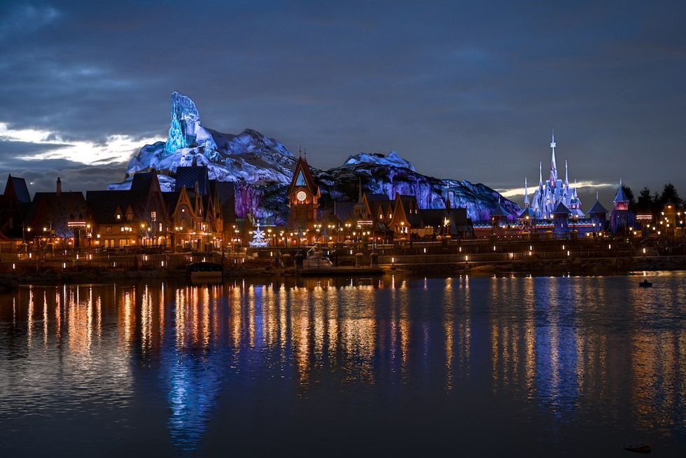 Illuminated fairytale village and castle reflected in a lake at dusk.