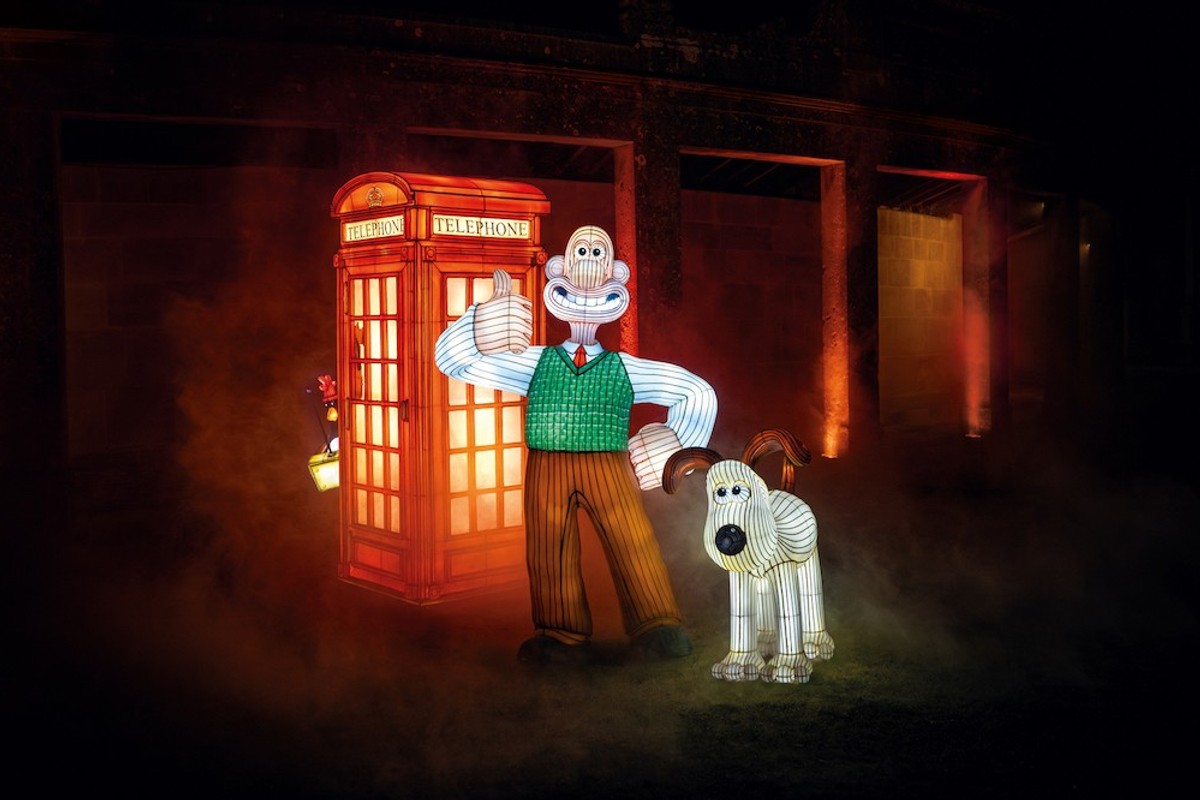 Illuminated figures of a man and dog with a red phone booth in a foggy, night setting.