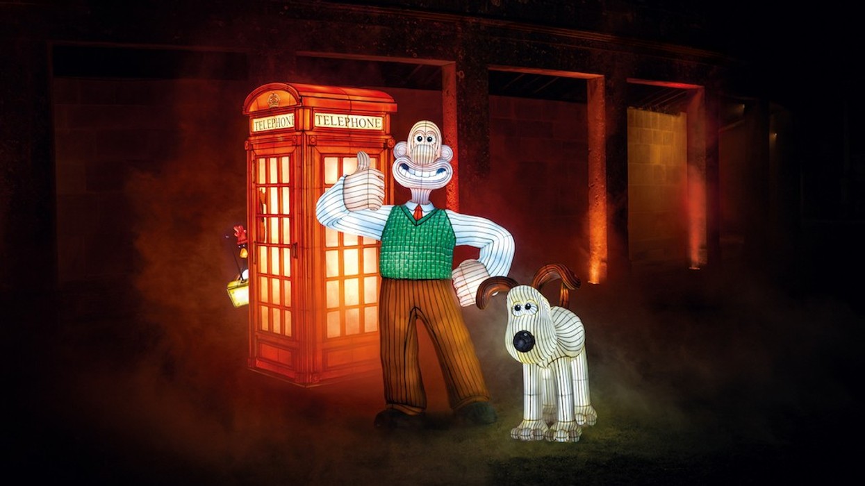 Illuminated figures of a man and dog with a red phone booth in a foggy, night setting.
