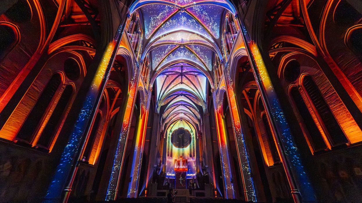Illuminated Garce Cathedral interior with colorful light projections on vaulted ceiling, AURA by Moment Factory