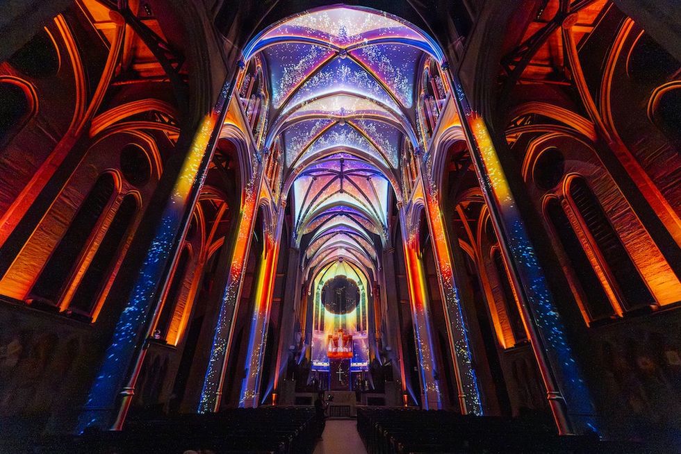 Illuminated Garce Cathedral interior with colorful light projections on vaulted ceiling, AURA by Moment Factory