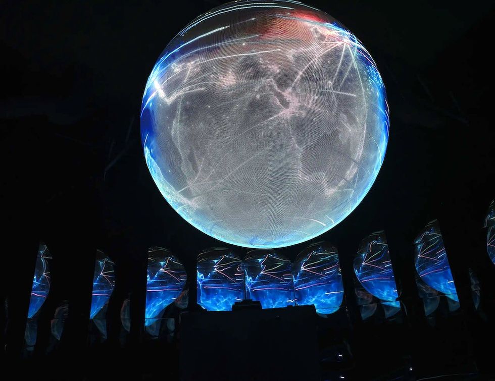 Illuminated globe with network lines, surrounded by reflective screens in a dark room.