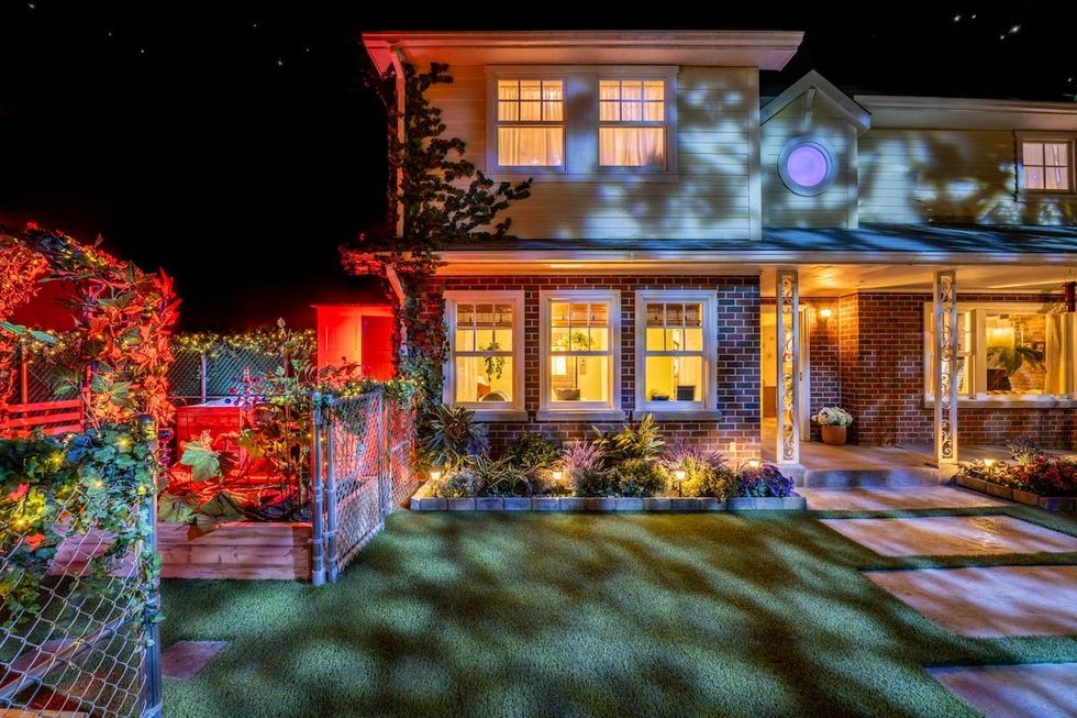 Illuminated house at night with garden and colorful lighting effects.