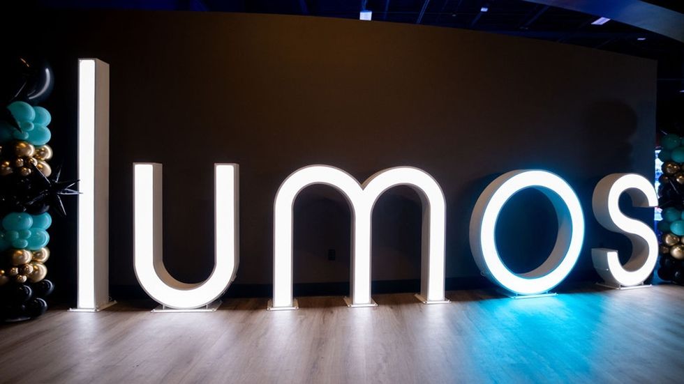 Illuminated "lumos" sign with colorful balloons on a dark background.