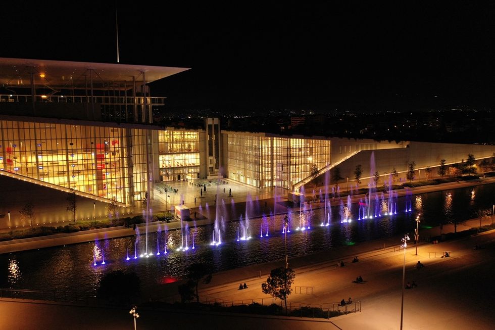 Illuminated modern building with colorful fountains at night.