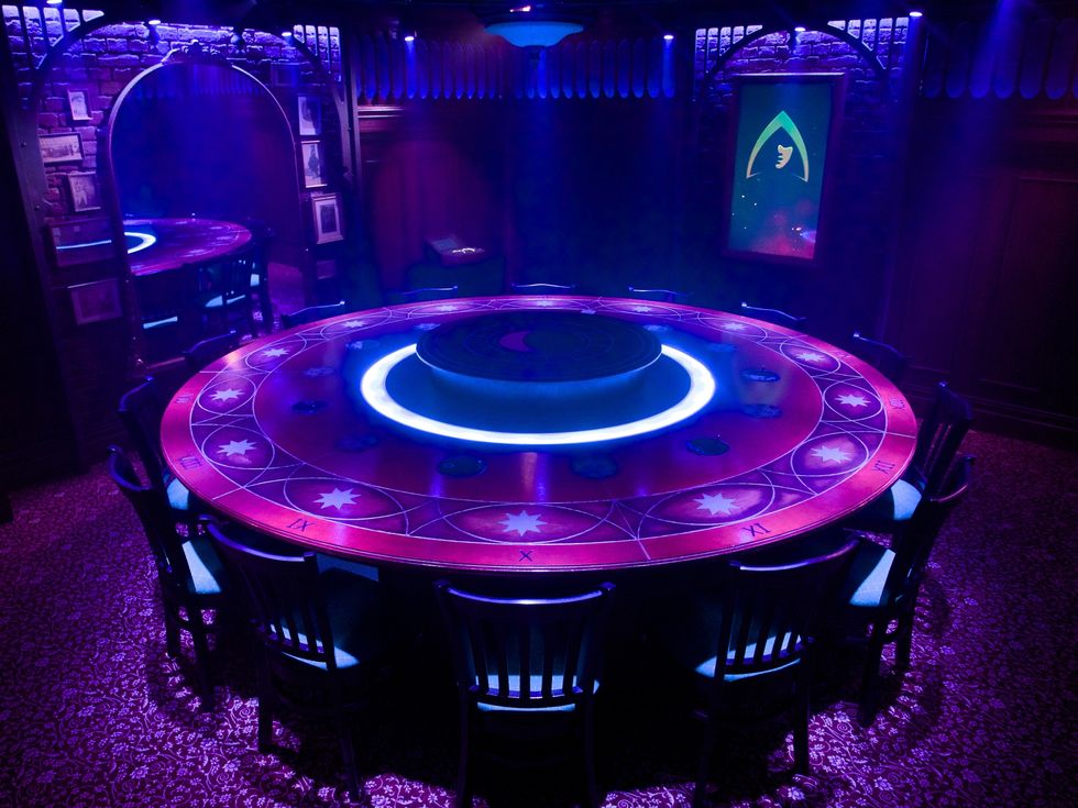 Illuminated, mystical round table with purple glow and chairs in a dimly lit room.
