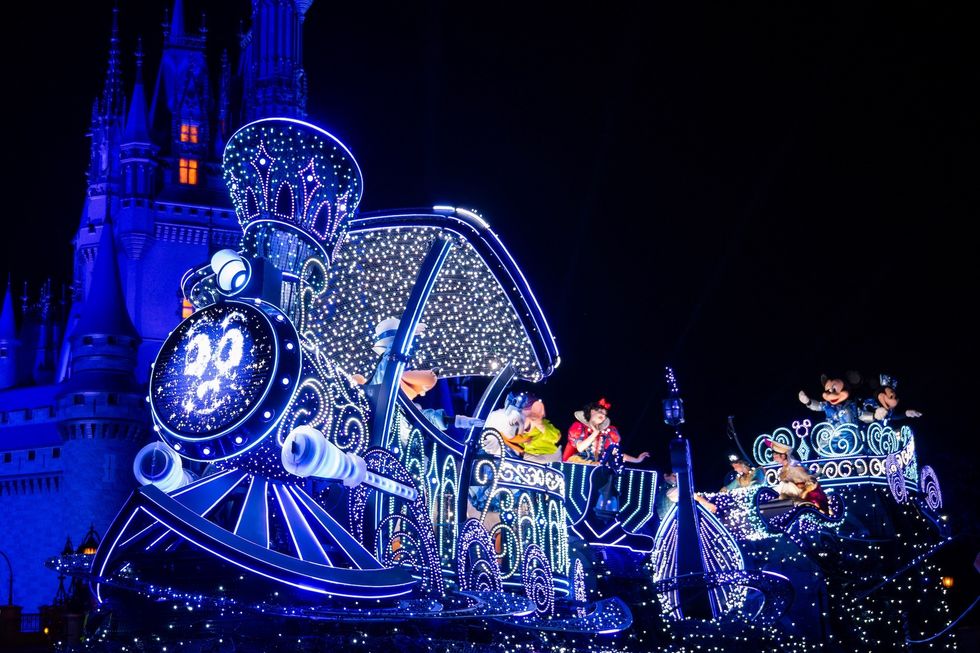 Illuminated parade float with characters in front of a castle at night.