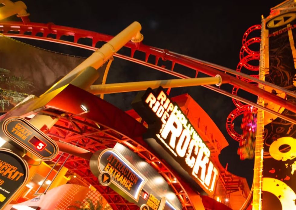 Illuminated roller coaster entrance at night, with visible loops and vibrant colors.