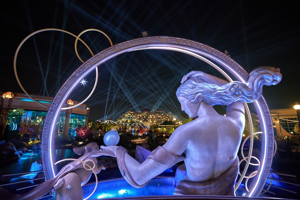 Illuminated statue with beams, arches, and a building in the background at night at Epic Universe