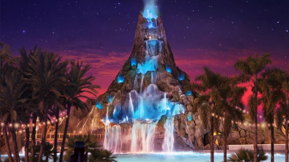 Illuminated waterfall on a rocky structure, framed by palm trees against a twilight sky at Universal's Volcano Bay
