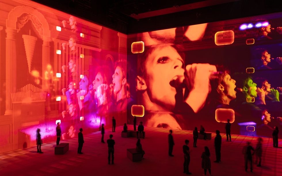 Immersive art installation with vivid projections of a singer on glowing orange walls.