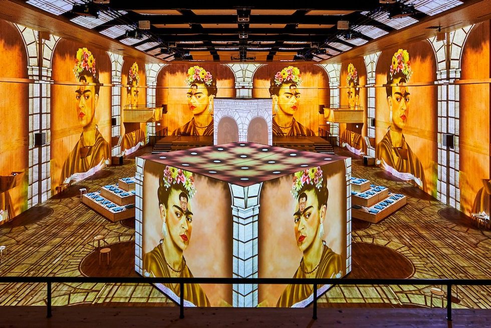 Immersive room with large portraits projected on walls and structures, featuring floral decor.