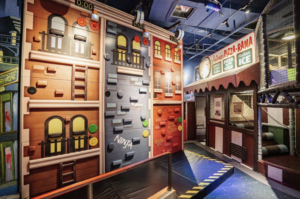 Indoor climbing attraction at Nickelodeon Playtime 2.0, with colourful building facades, safety barriers, and a pizza-themed storefront.