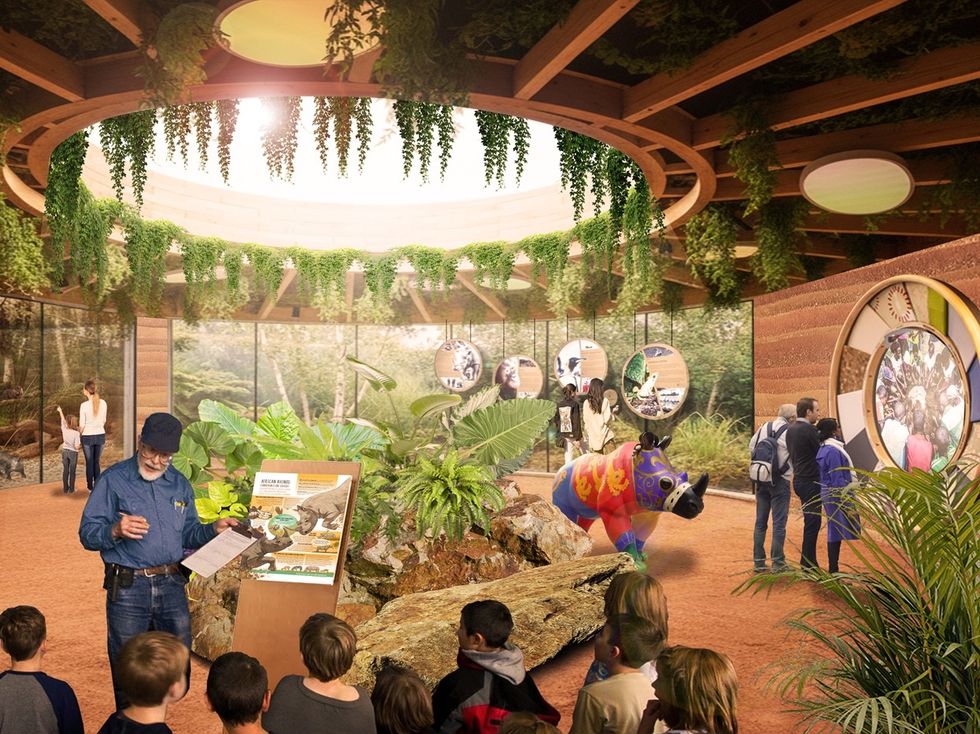 Indoor exhibit at Odense Zoo with plants, educational displays, and people observing a colorful animal statue.