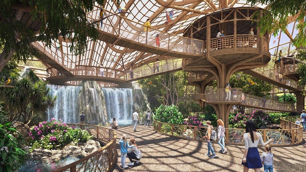 Indoor garden with waterfall, wooden walkways, lush plants, and people exploring.