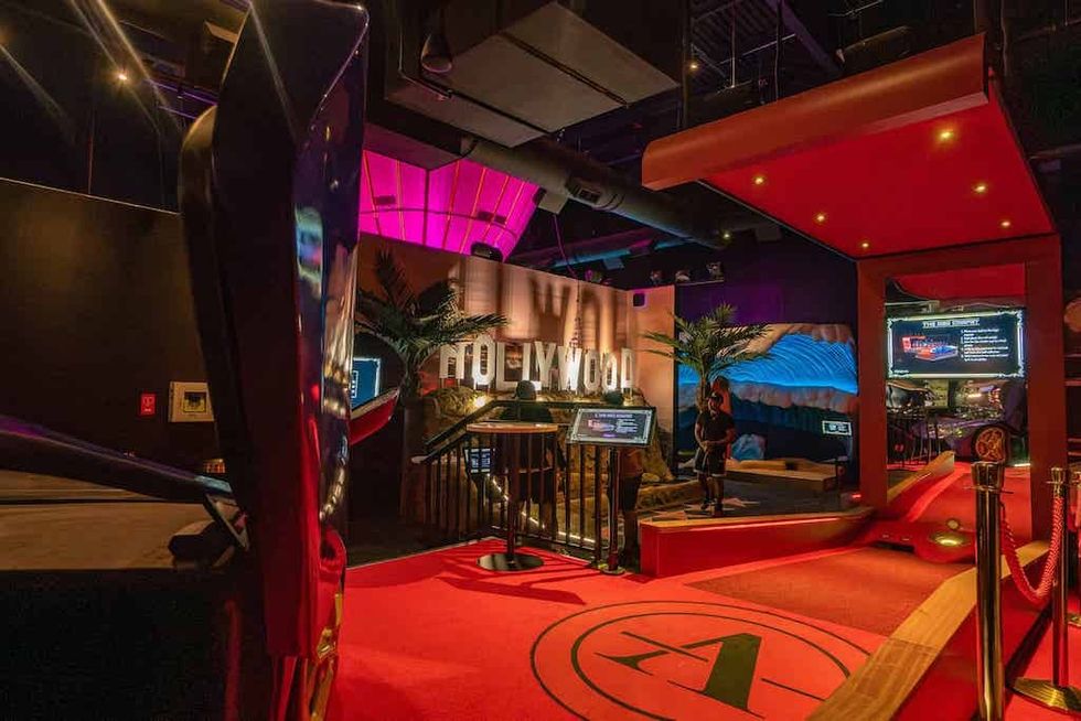 Indoor mini-golf course with Hollywood theme, red carpet, and illuminated screens.