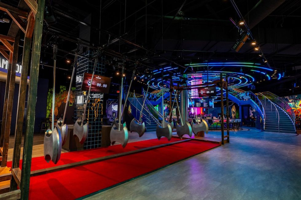 Indoor obstacle course with swinging axes and neon lights.