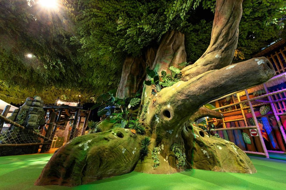 Indoor playground with a large artificial tree and vibrant foliage.