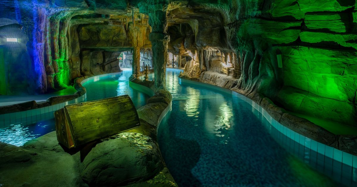 Indoor pool in a cave-like setting with colourful lighting and a submerged treasure chest at Suntago Water World.