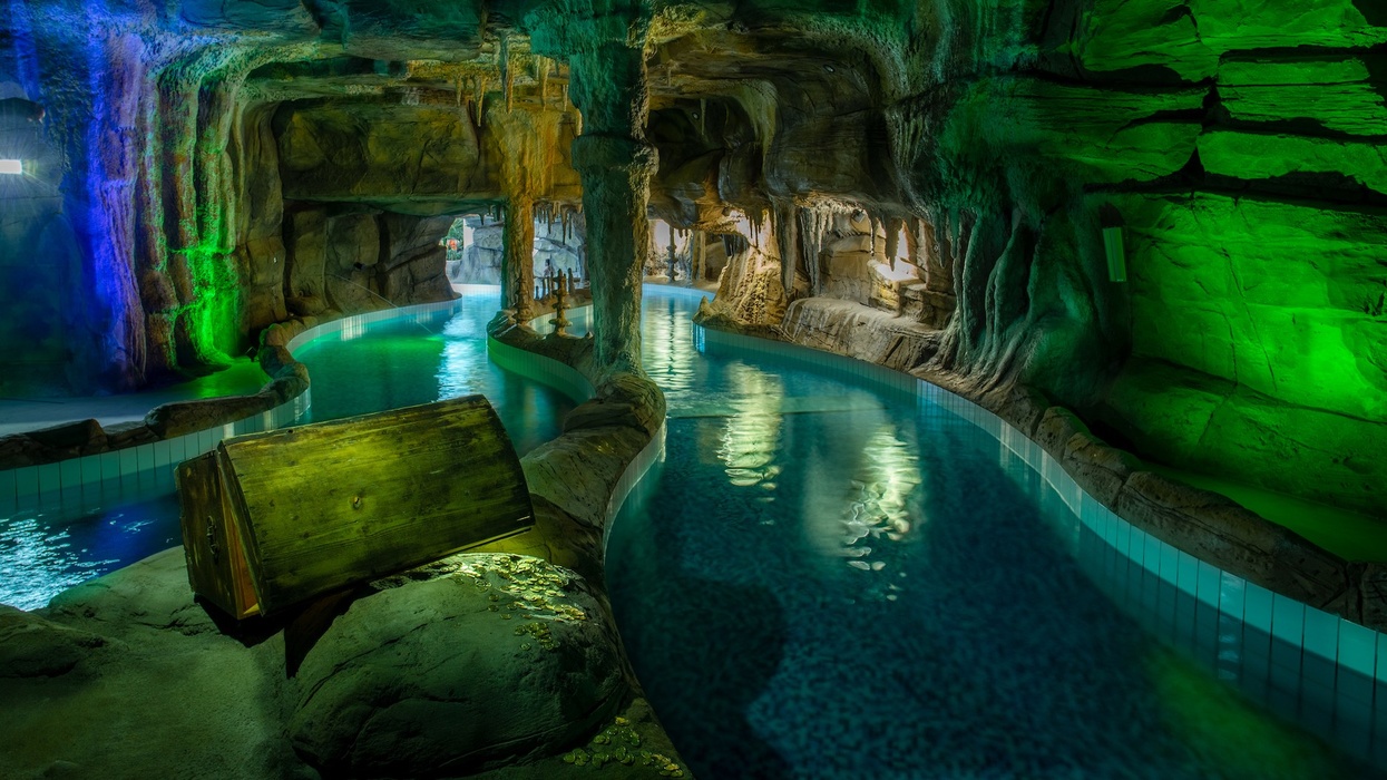 Indoor pool in a cave-like setting with colourful lighting and a submerged treasure chest at Suntago Water World.