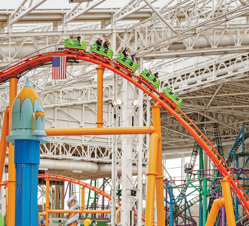 Indoor roller coaster with green cars and an American flag under a large steel structure.