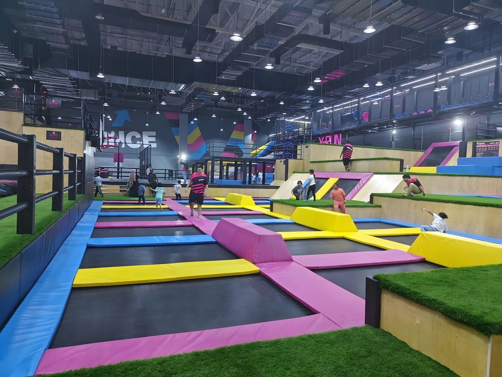 Indoor trampoline park with colorful mats and ramps, people playing and jumping.