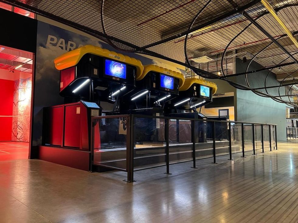 Indoor virtual reality ride with yellow seats and protective netting above.