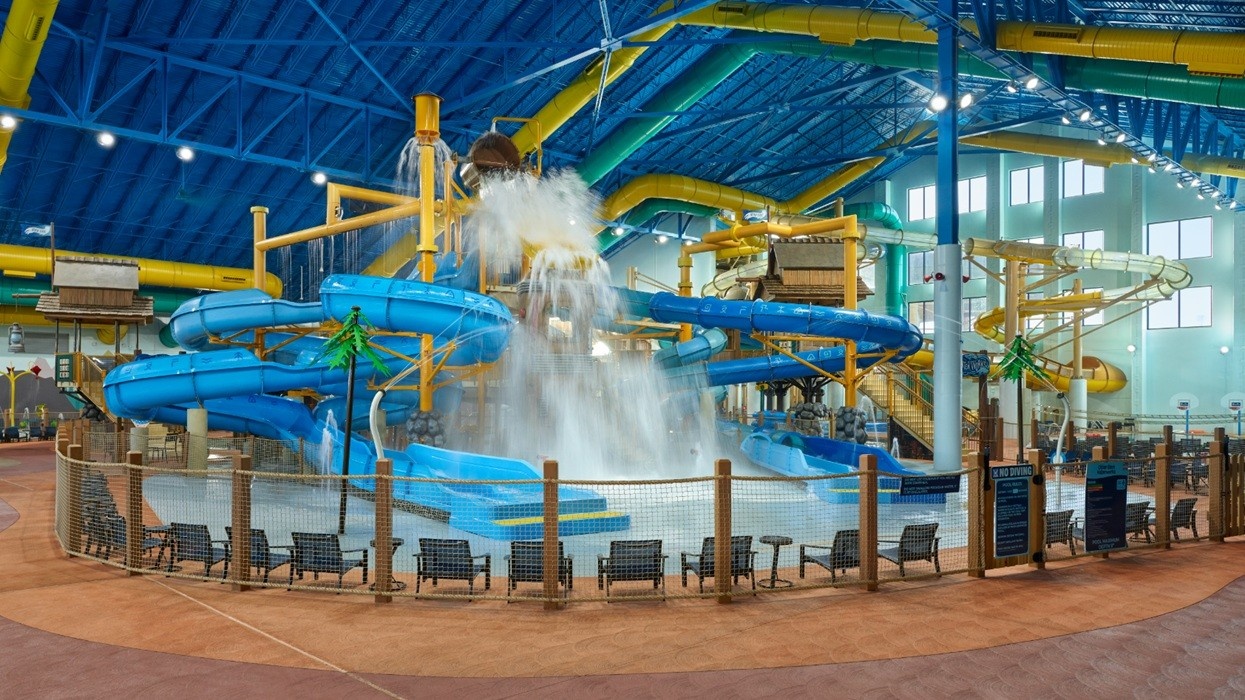 Indoor water park with blue slides and large dumping bucket.