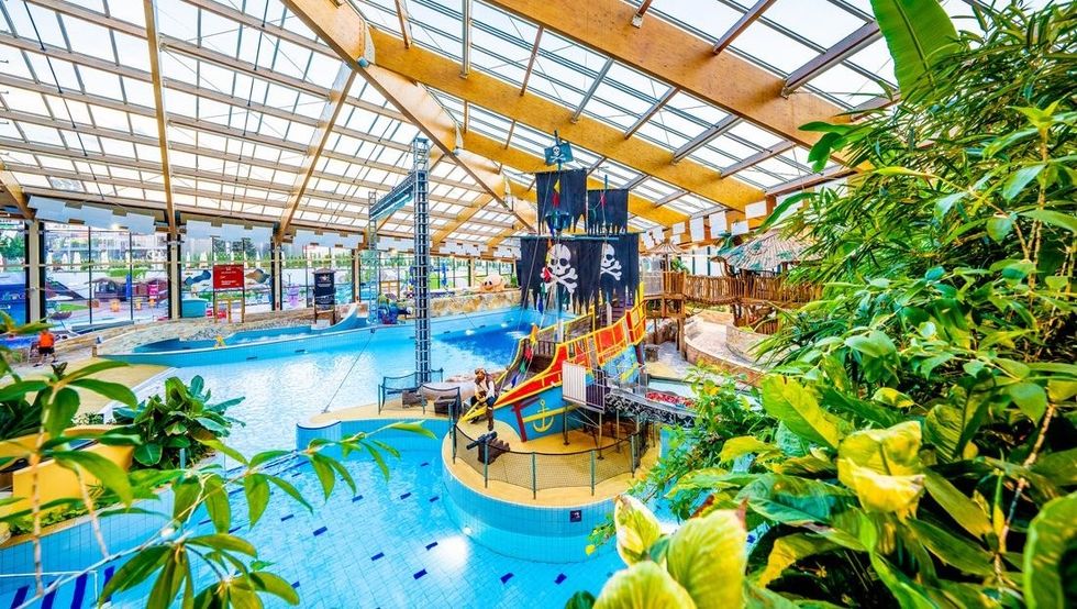 Indoor waterpark with pirate ship feature, surrounded by lush greenery and tall glass ceiling.