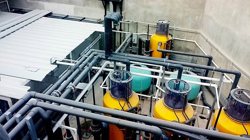 Industrial facility with yellow and blue tanks, interconnected pipes, and a metal roof.