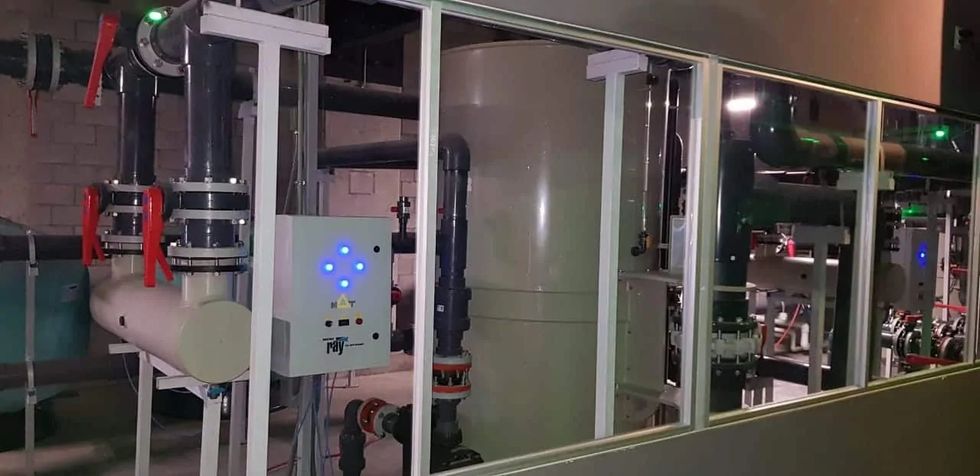 Industrial machinery room with large pipes, tanks, and a control panel with blue lights.
