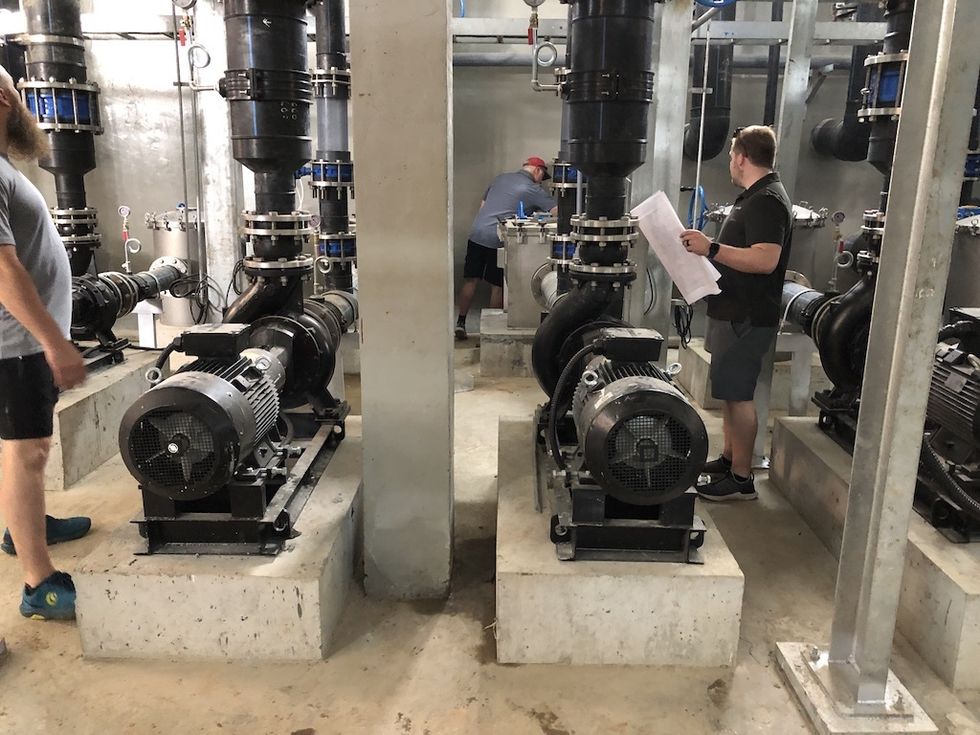Industrial pump room with workers inspecting machinery and pipes.