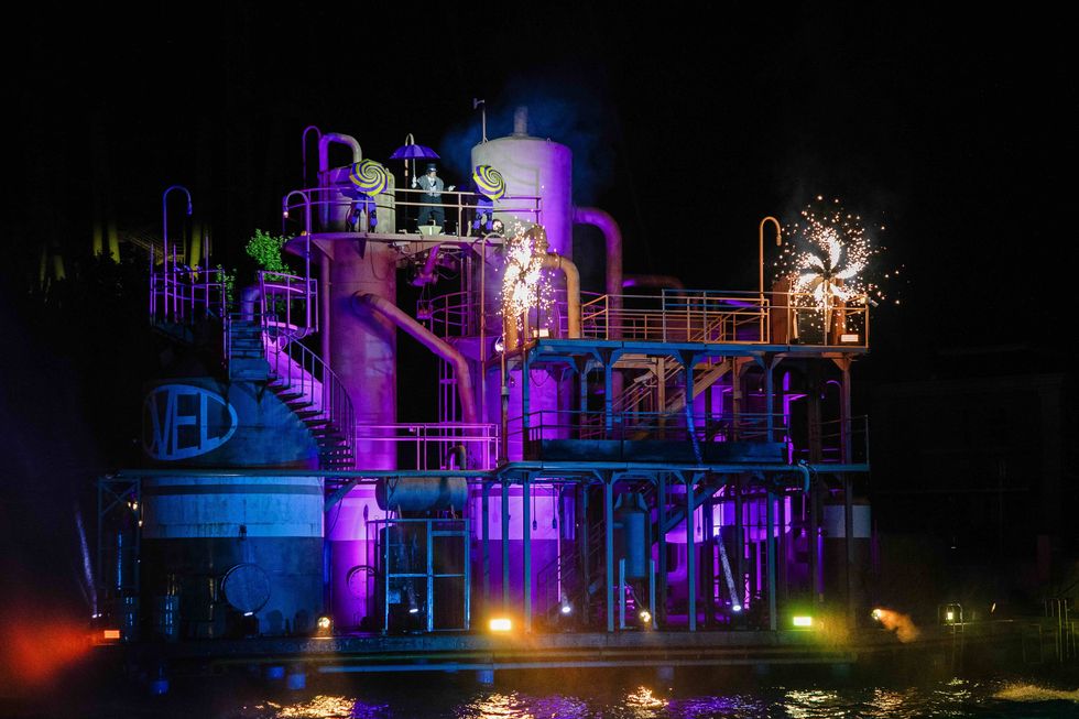 Industrial structure lit in purple with fireworks at night.