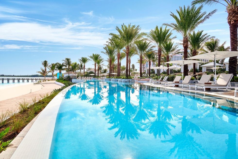 Infinity pool with palm trees, lounge chairs, and blue sky reflection.