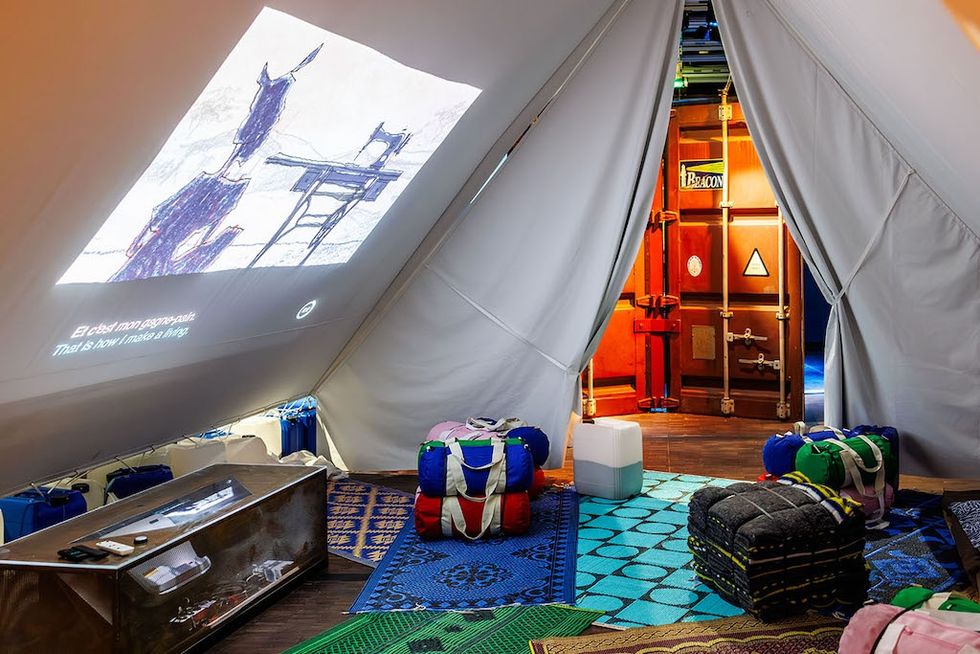 Inside a cozy tent with projection, colorful bags, and vibrant rugs on the floor.