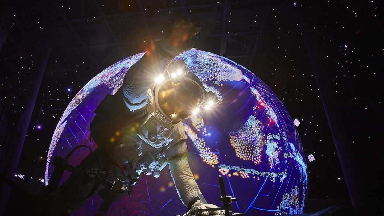 Inside Alif – The Mobility Pavilion, Astronaut reaches towards a colorful, illuminated Earth model in a starry, dark setting.