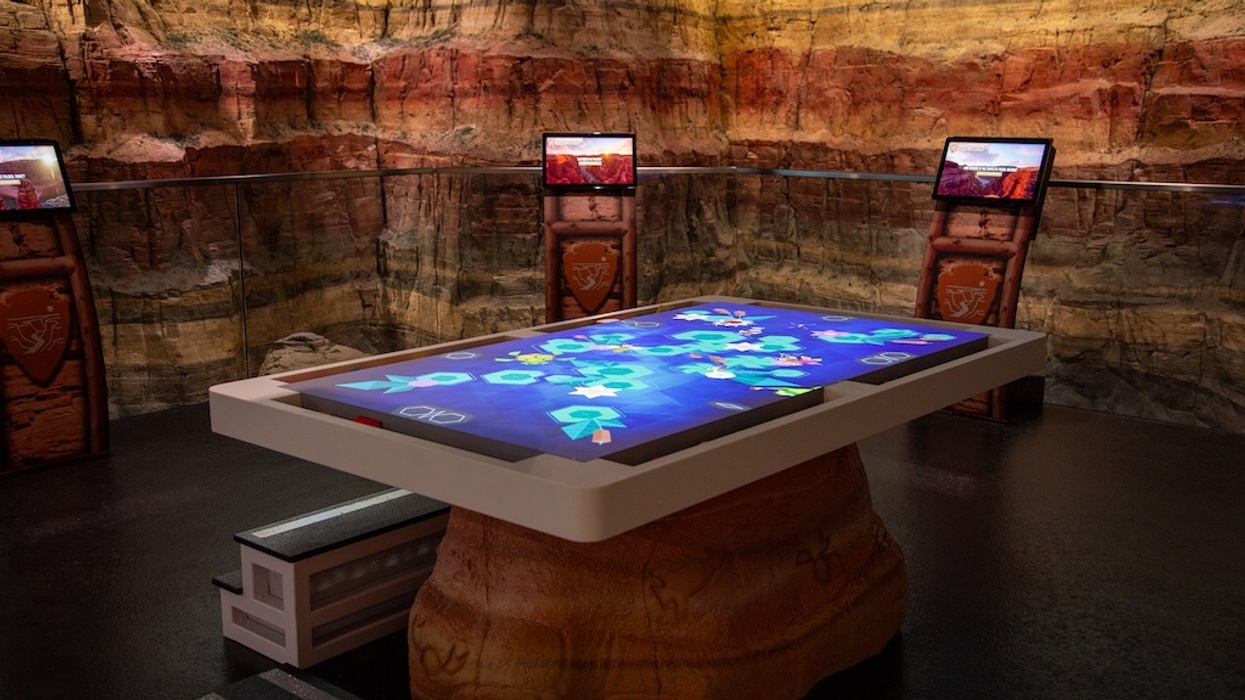 Interactive digital table in a canyon-themed room with screens on the walls.