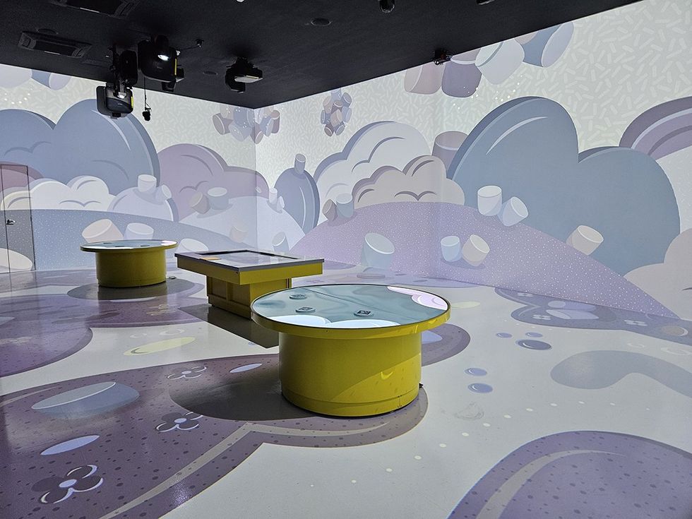 Interactive room with purple cloud murals and circular yellow tables.