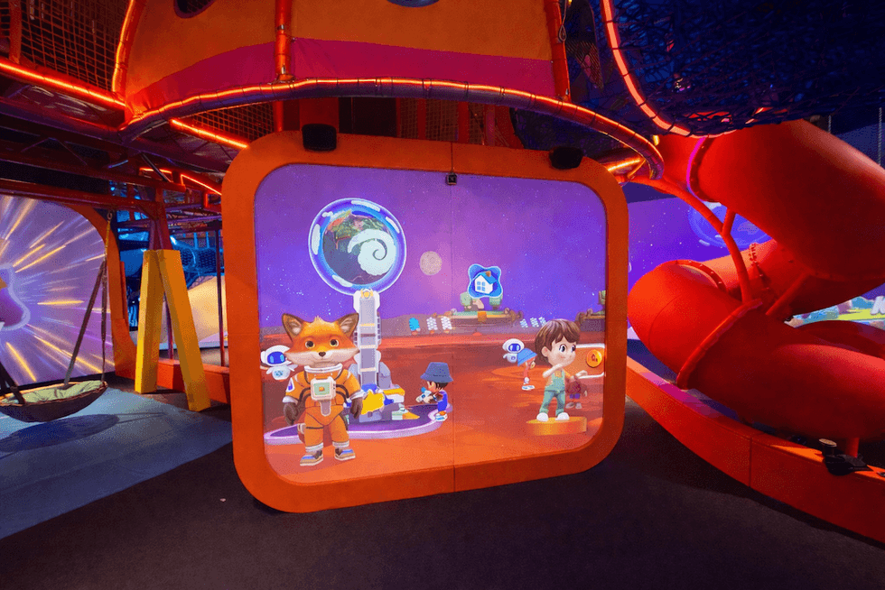 Interactive screen at Hello Park with animated fox and boy in a colorful play area.