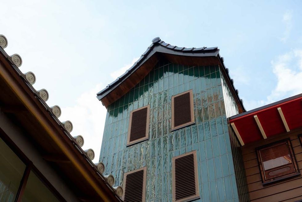 Japanese-style building with green tiles and wooden shutters under a blue sky.