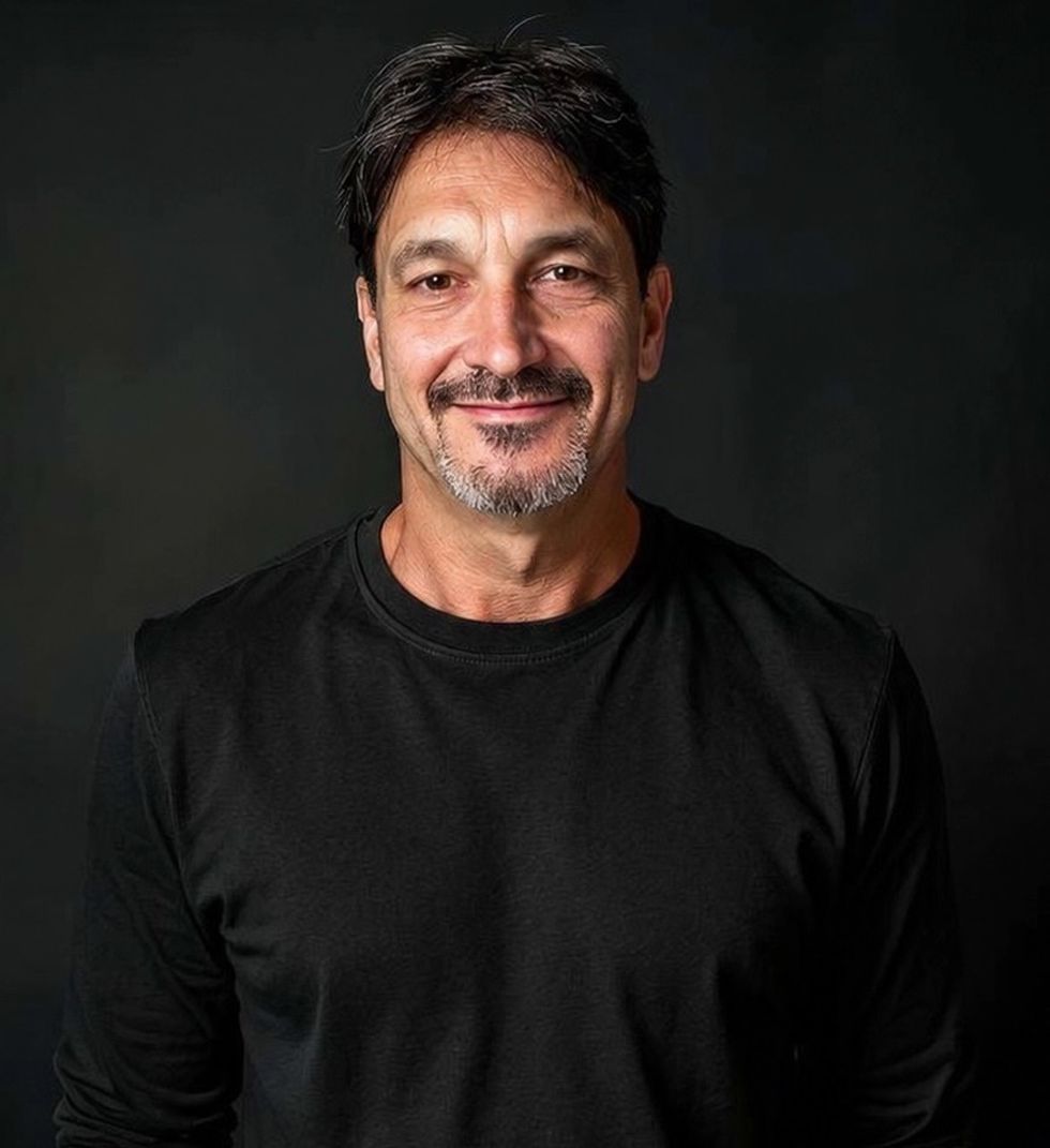 John Miceli headshot Smiling man with short hair and a goatee, wearing a black shirt, on a dark background.
