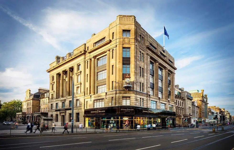 Johnnie Walker Experience in a historic stone building on a city street, with blue skies and a small crowd passing by
