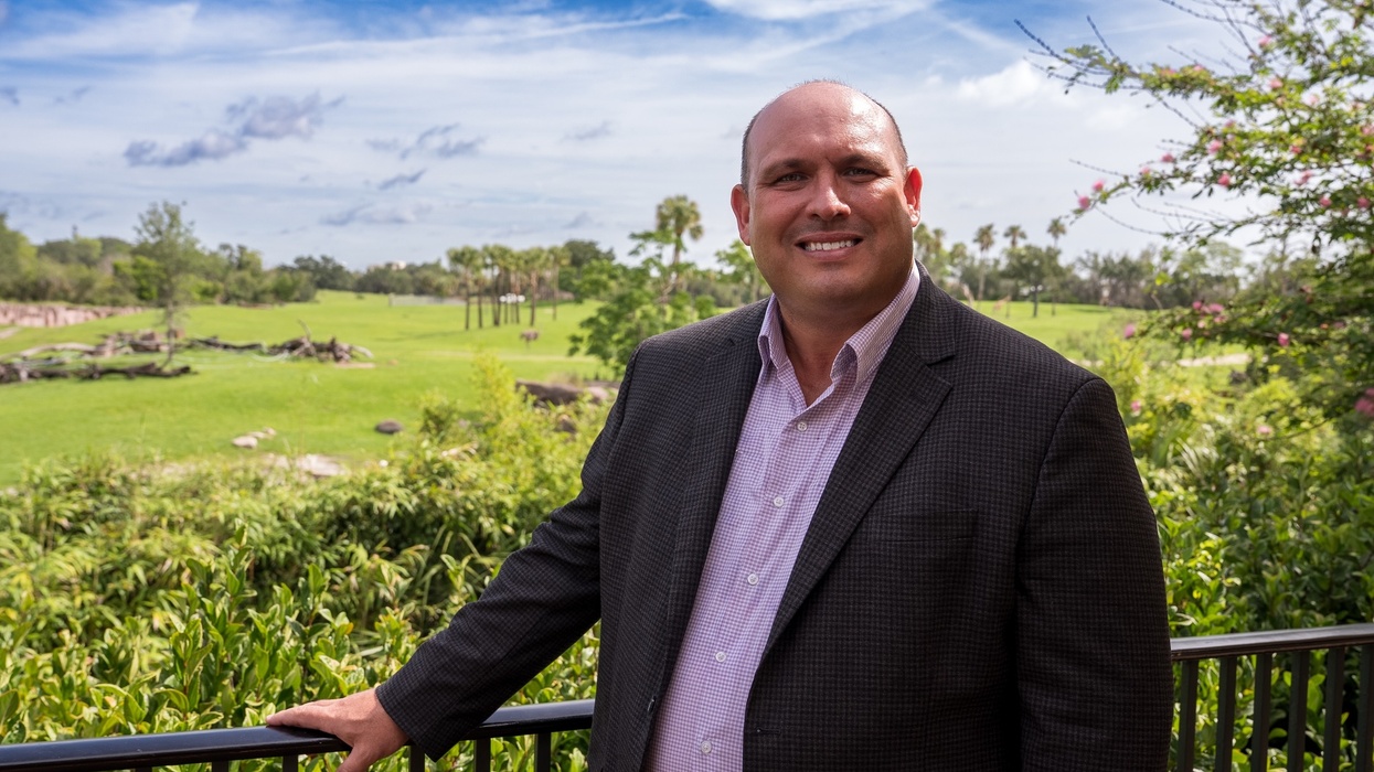 Jon Vigue in a suit smiling outdoors with a scenic green landscape in the background at Busch Gardens Tampa Bay