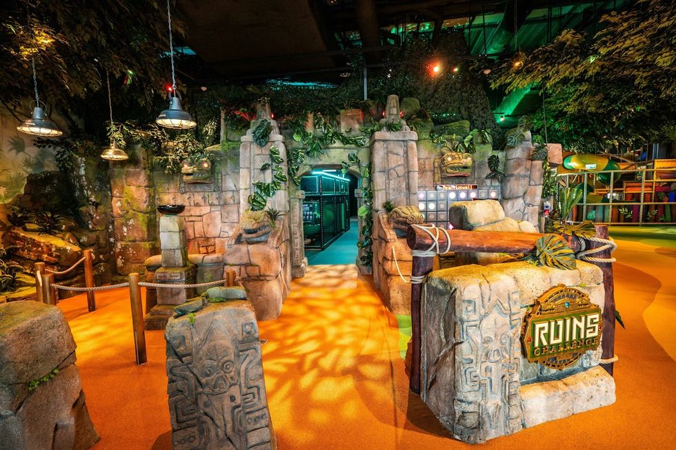 Jungle-themed indoor adventure park with stone ruins and lush foliage.