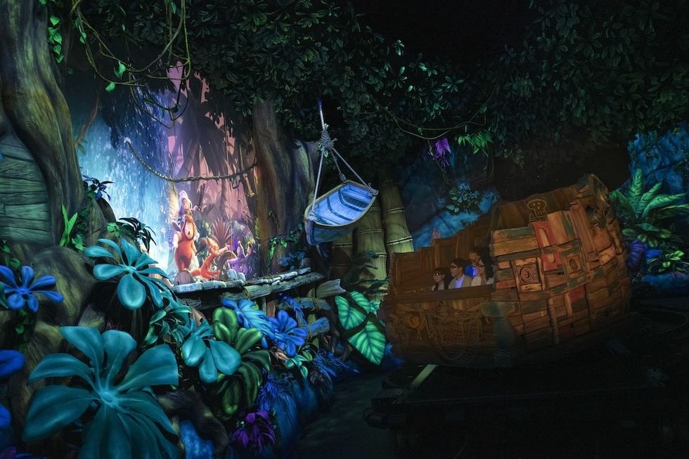 Jungle-themed ride, Peter Pan\u2019s Never Land Adventure at Tokyo DisneySea, with vibrant foliage and three people in a boat-like ride vehicle.